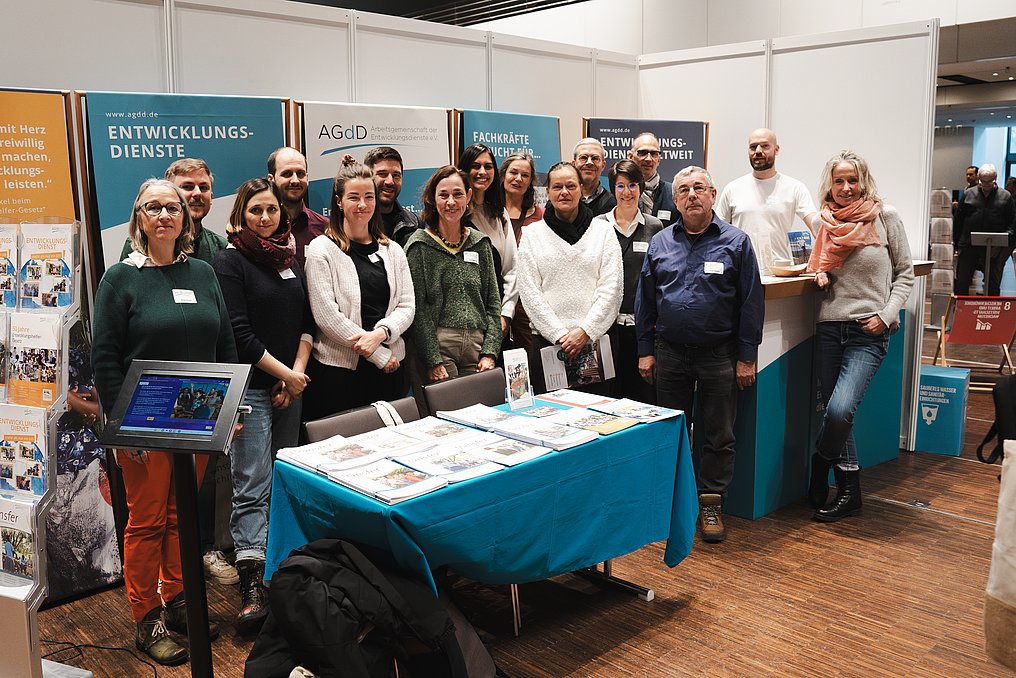 14 Personen stehen vor Rollups mit der Aufschrift AGdD an einem Messestand. 